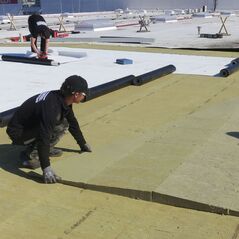 Szakember ROCKWOOL lejtésképző kőzetgyapot lapot fektet egy lapostető szigetelésekor.